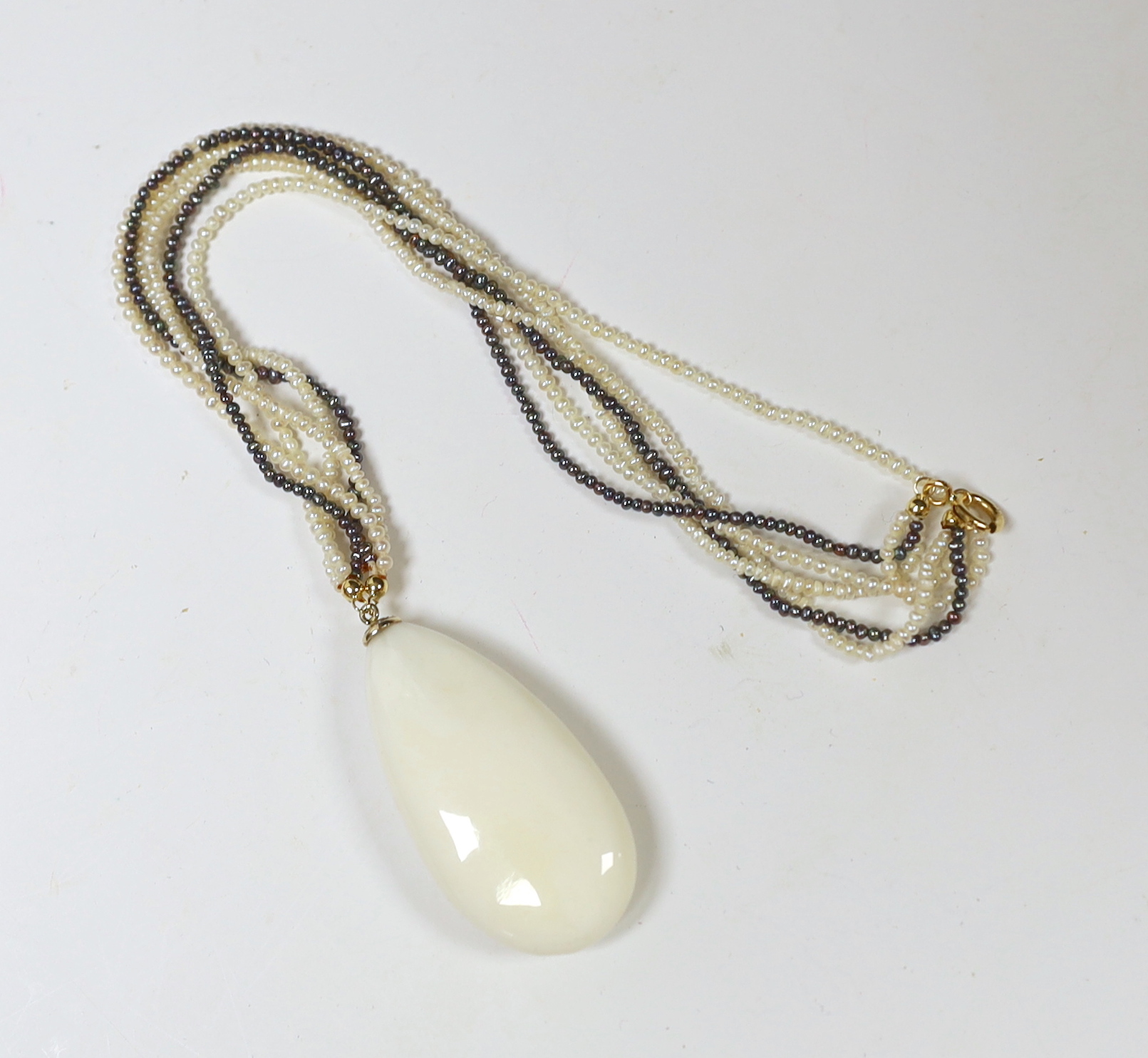 A yellow metal mounted pear shaped white coral pendant, with diamond chip set bale, 45mm, on a triple strand two colour seed pearl necklace, with 750 yellow metal clasp, 40cm.